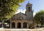 Fachada principal de la Iglesia de Santa Cristina de Lavadores rodeada de frondosos árboles verdes