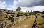 Ruinas del castro con un árbol solitario en la colina bajo un cielo parcialmente nublado