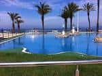 Piscina exterior con palmeras y vistas al mar en Samil