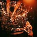 DJ actuando en el escenario con luces cálidas y público