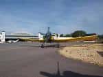Avión amarillo en la pista de aterrizaje con hangar al fondo