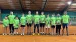Grupo de jugadores y entrenadores en una pista de tenis cubierta