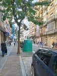 Vista de la calle Benito Corbal con árboles, personas y un coche aparcado.