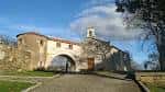 Vista exterior de la Capilla de San Roque y su arco de entrada bajo un cielo azul.