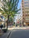 Perspectiva de la calle Benito Corbal con árboles y transeúntes.