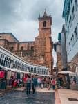 Vista de la torre de la iglesia en una calle peatonal con puestos de mercado o arcadas cubiertas
