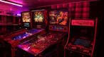 Interior del local con máquinas recreativas y pinball bajo iluminación magenta