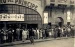 Vista exterior histórica en blanco y negro de la entrada del cine con gente haciendo cola