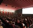 Interior de una sala de cine con butacas rojas y público, adecuada para eventos