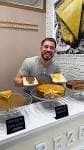 Hombre sonriente mostrando una variedad de tartas de queso en el mostrador de Suárez Cake
