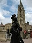 Primer plano de la escultura de La Regenta con la torre gótica de la Catedral de Oviedo