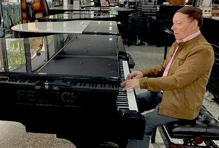 Hombre tocando un piano de cola en el showroom de instrumentos