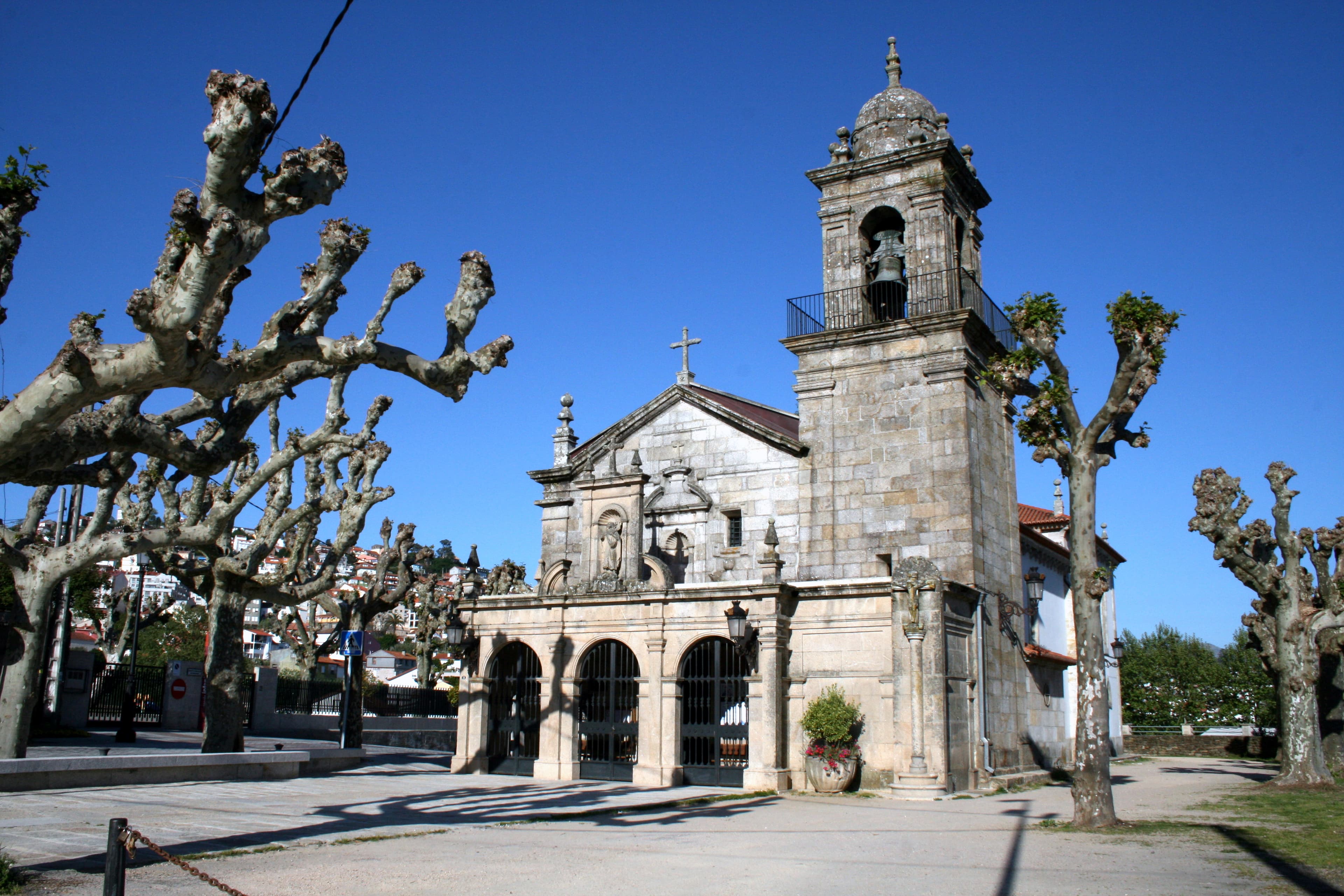 Vista exterior de la Iglesia de Santa Cristina de Lavadores bajo cielo azul con árboles sin hojas