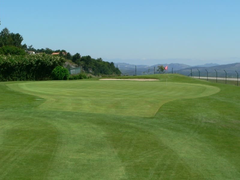 Green del campo de golf con bandera y paisaje de fondo