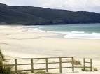 Playa de arena con valla de madera y olas suaves en Doniños