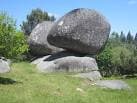 Roca equilibrada de Penas de Rodas en un paisaje de hierba y árboles
