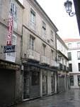 Edificio de piedra con balcones y comercios en una calle de Ourense