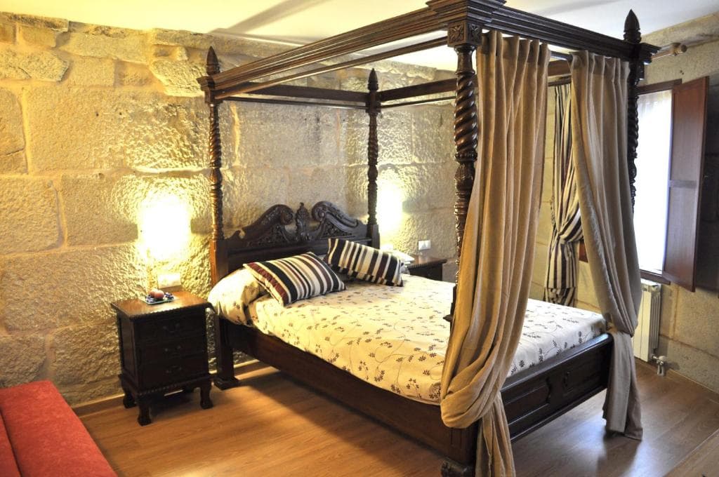 Habitación de hotel con cama con dosel y pared de piedra vista