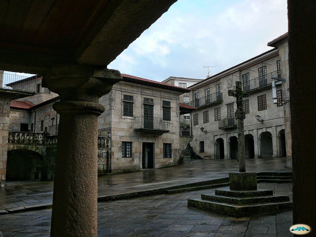 Plaza histórica con cruceiro y edificios de piedra bajo un cielo nublado