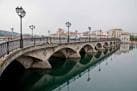 Puente del Burgo con farolas y reflejos en el agua en un día gris