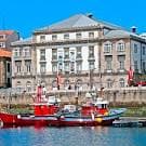 Vista exterior del Teatro Rosalía de Castro desde la ría, con barcos en primer plano