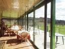 Salón acristalado o terraza interior con mesas y vistas al campo de golf.