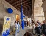 Evento al aire libre bajo un pórtico con personas y una bandera de la Unión Europea
