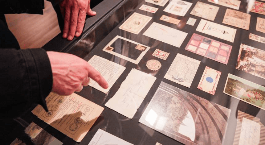 Detalle de una exposición con objetos históricos bajo cristal y manos señalando