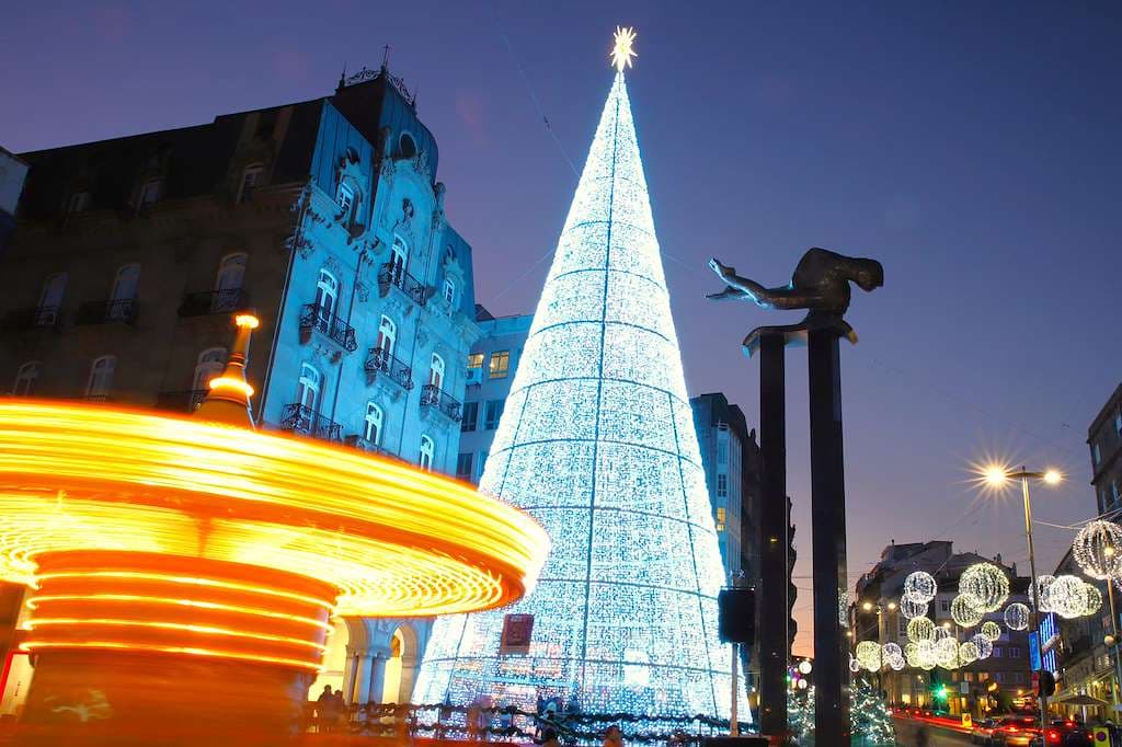 Árbol de Navidad iluminado y carrusel en una plaza de Vigo por la noche