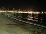 Playa de Orzán de noche con las luces de la ciudad reflejadas en la arena mojada