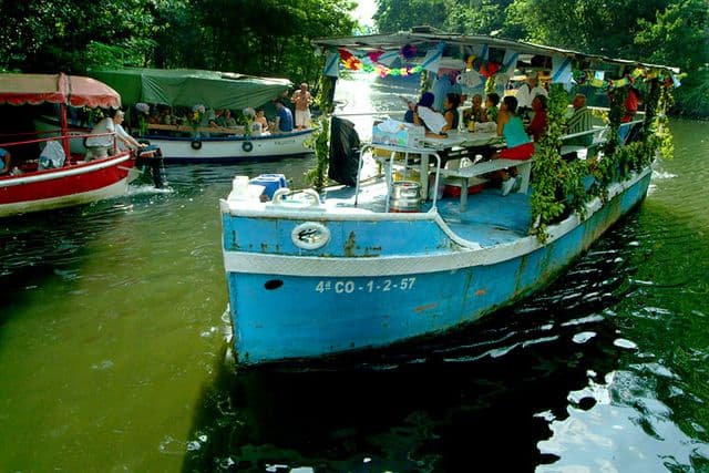Barcos con asistentes navegando por el río durante la Romaría de Os Caneiros