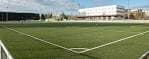 Campo de fútbol de césped artificial en el Complejo Manolo Barreiro con edificios al fondo.