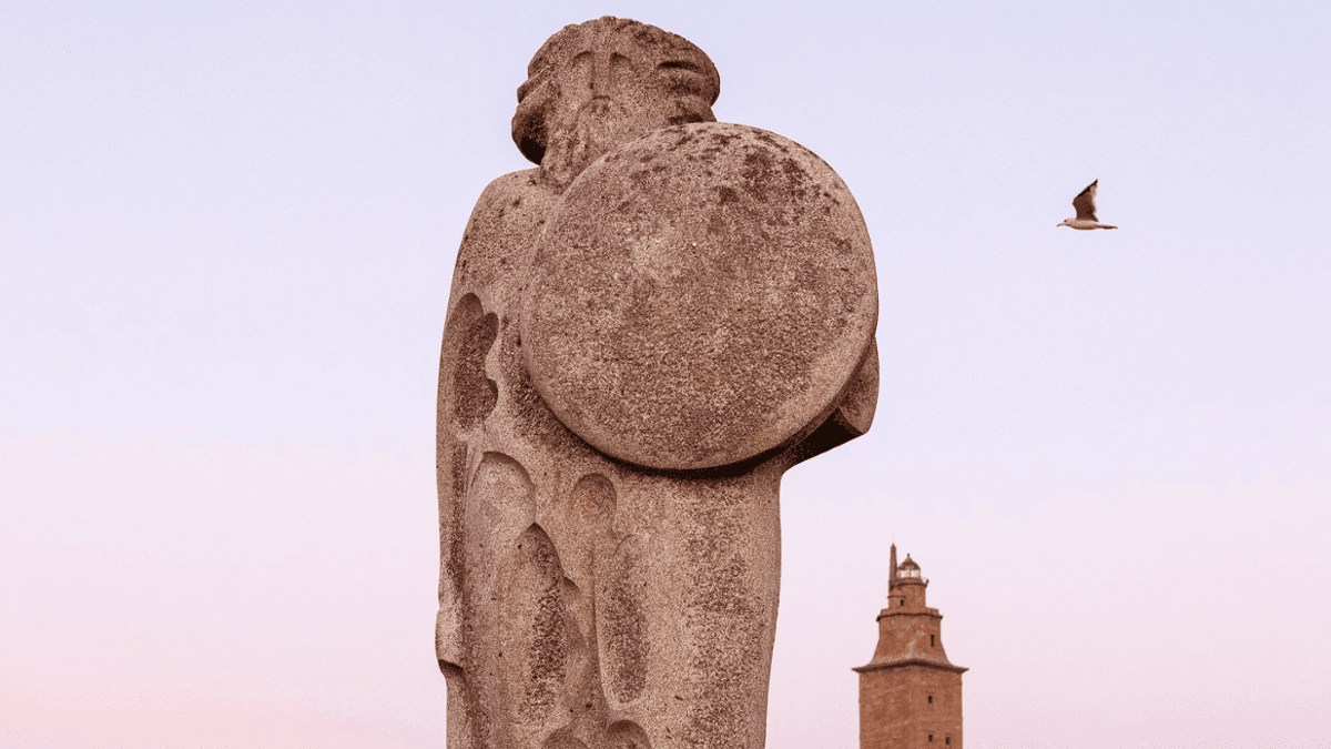 Estatua de Breogán con la Torre de Hércules al fondo al atardecer