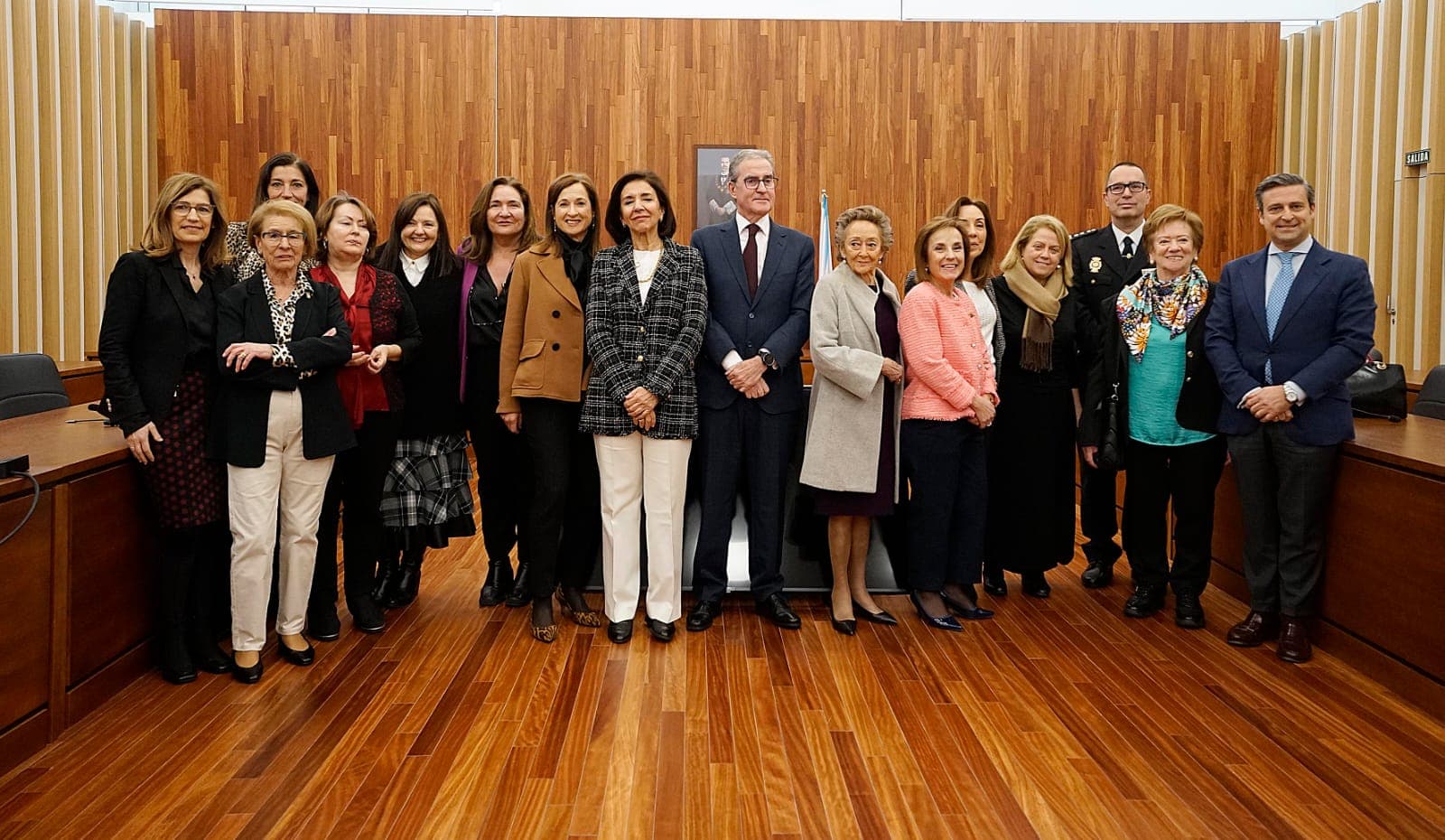 Grupo de personas en un evento formal dentro de una sala con paneles de madera