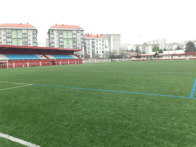 Vista del campo de fútbol con gradas y edificios al fondo