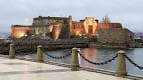 Castillo de San Antón iluminado al anochecer desde el paseo marítimo
