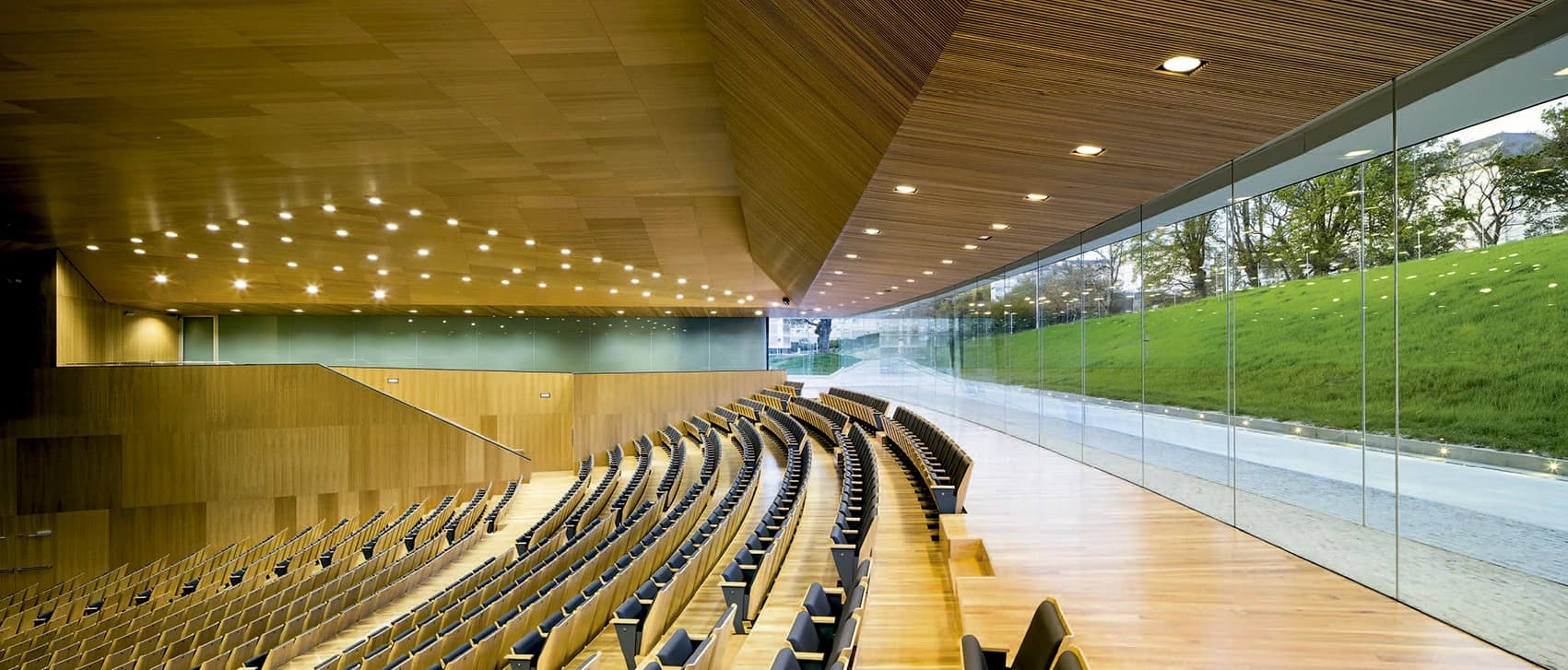 Interior del auditorio con asientos de madera y ventanales