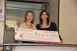 Dos mujeres presentando un cheque de donación en un evento benéfico.