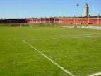 Campo de fútbol con la valla perimetral roja y una torre al fondo