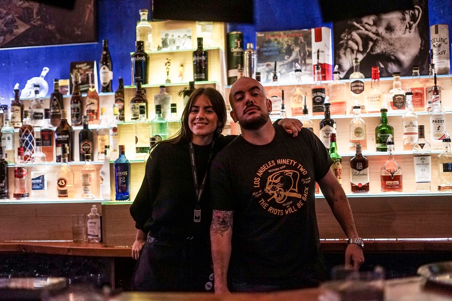 Dos miembros del personal posando detrás de la barra bien surtida del pub
