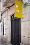 Entrada principal de MUTA con cartel amarillo en fachada de piedra
