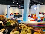 Vista del área de catering y buffet con la zona de asientos de colores al fondo
