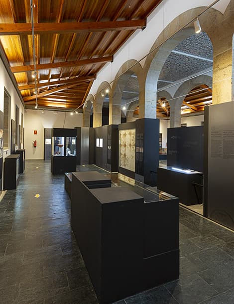 Interior de la Sala de Exposicións Porta Miñá con expositores y techo de madera