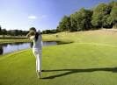 Jugadora de golf realizando un swing en el campo, con un lago al fondo.