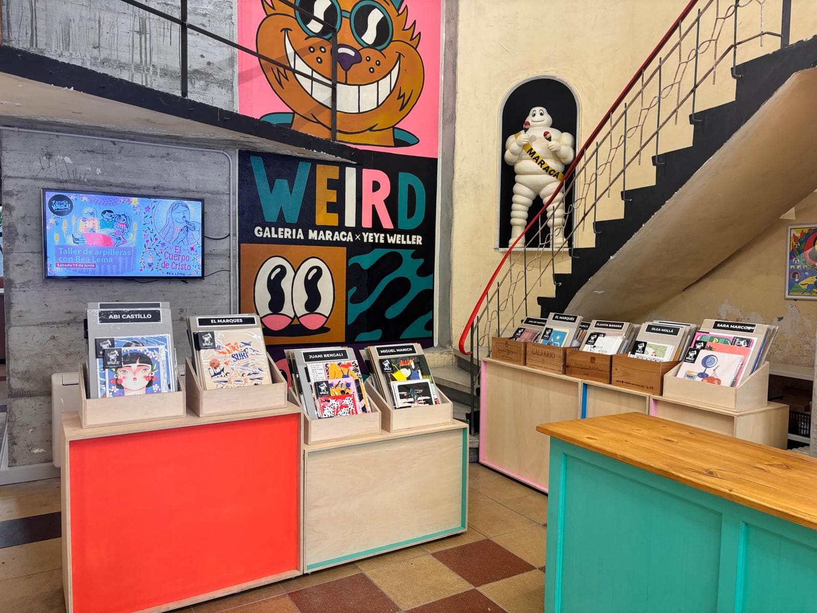 Zona de exposición y escalera en Galería Maraca con murales artísticos
