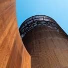 Perspectiva ascendente de una torre cilíndrica de acero corten bajo cielo azul