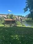 Área de césped con un banco y el Puente Romano al fondo en Ourense