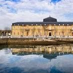 Gran edificio histórico junto al agua con reflejos, parte del complejo del Arsenal