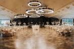 Gran salón interior de eventos con mesas redondas y lámparas modernas.