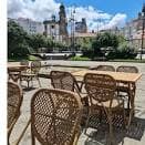 Terraza vacía de la Taberna Kamelia con mobiliario de mimbre y edificios históricos al fondo